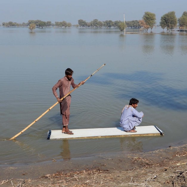 Zwei Männer auf einem Floss auf einem überschwemmten Feld in Pakistan 2022.